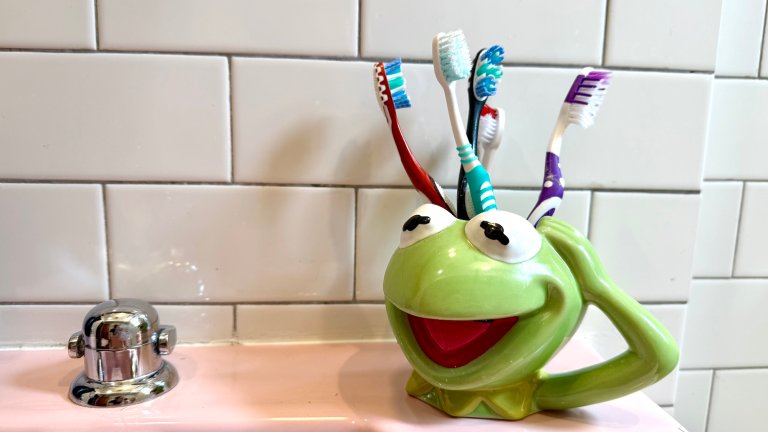 kermit cup with toothbrush in it on pink sink