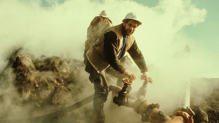 Two men in a steamy landscape with a pipe. One man has his hands on two valves.