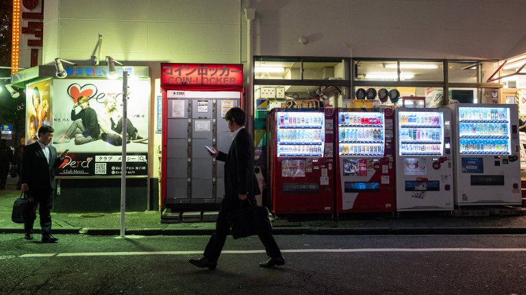 Japanese man walks past vending machines at night in Tokyo.