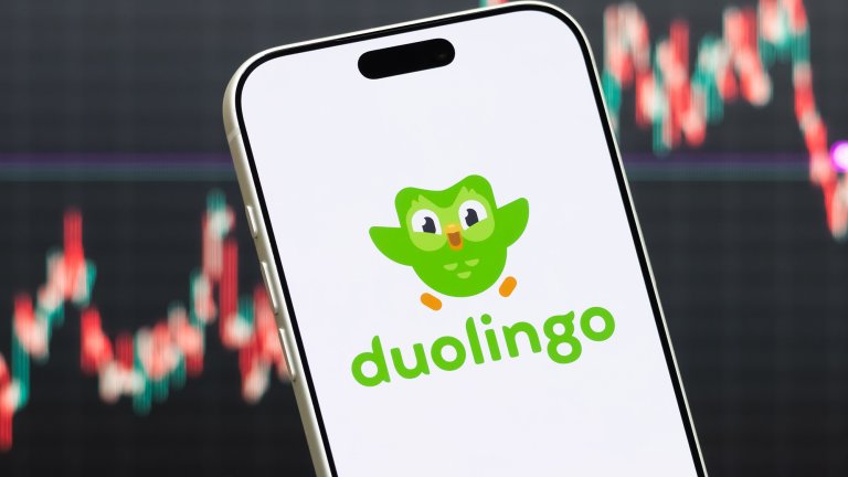Duolingo logo shown on smartphone with latest stock market chart in background.