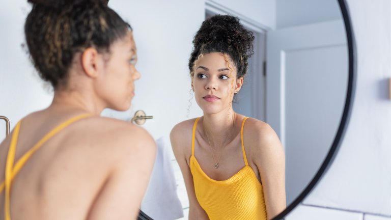 Young Black woman looking in bathroom mirror.