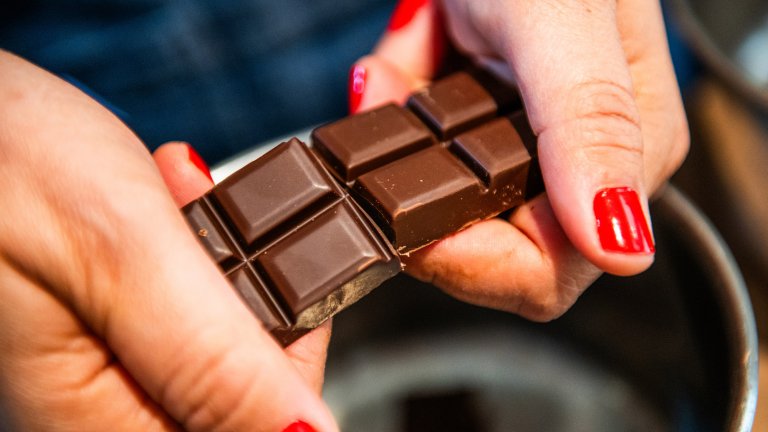Close up of hands with red nail polish breaking a piece of chocolate
