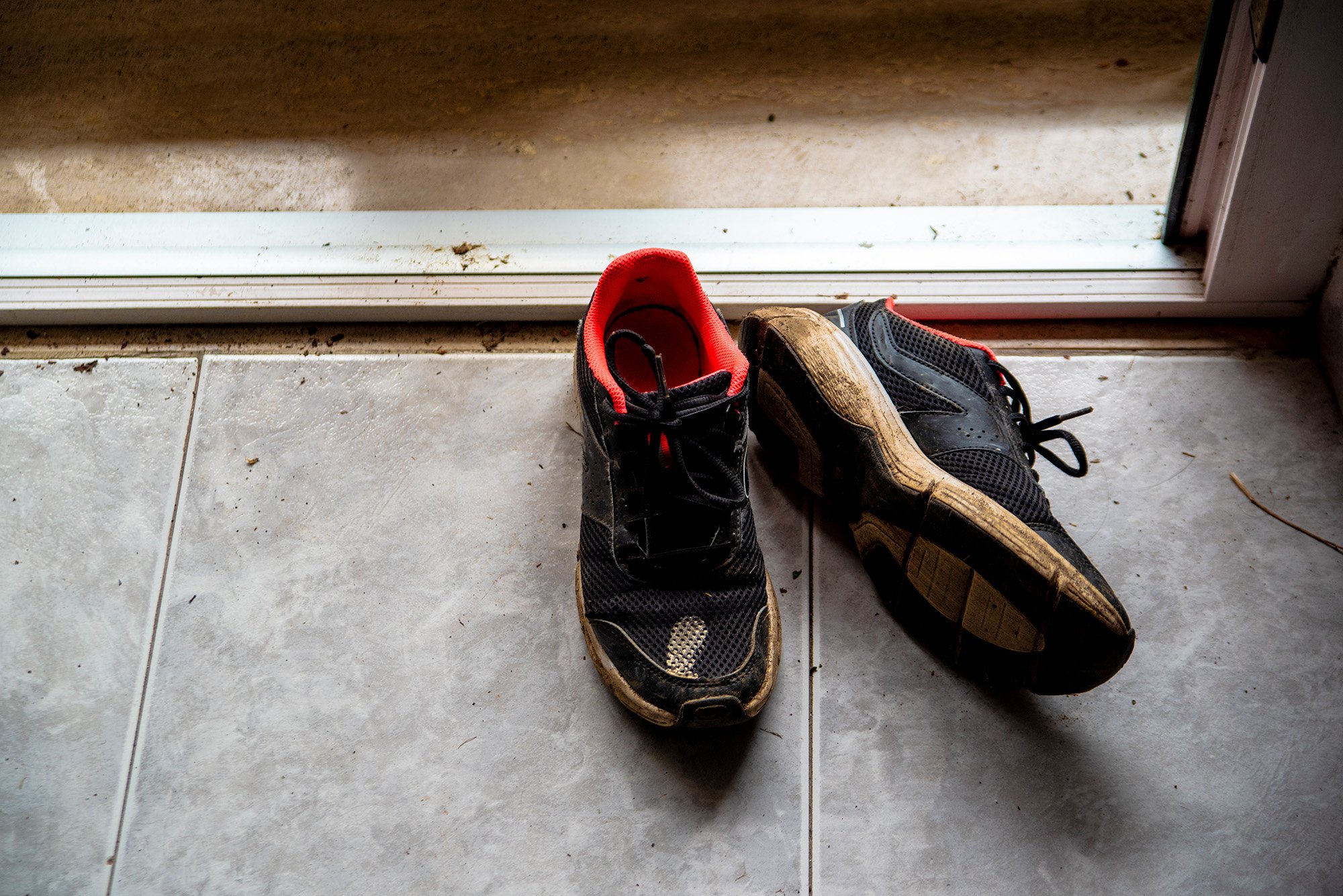 A pair of muddy sneakers sitting on the patio side of a sliding door