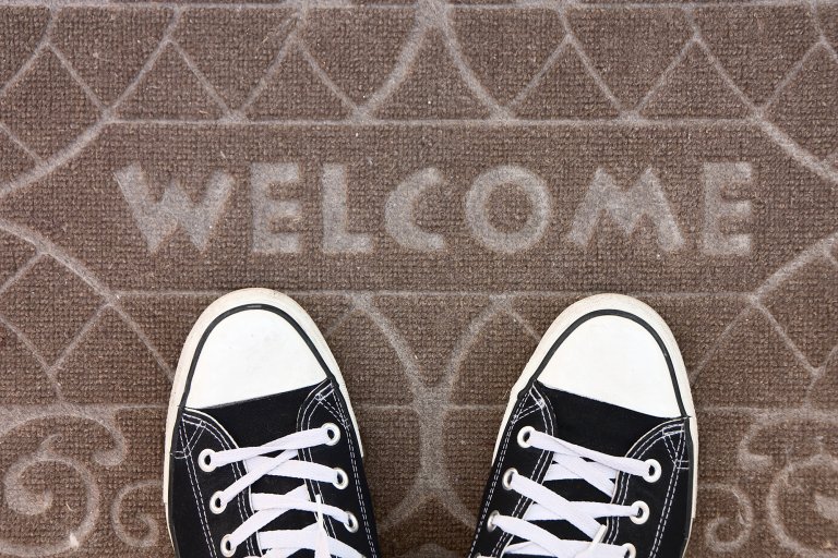 A pair of black Converse sneakers sitting on a beige welcome mat
