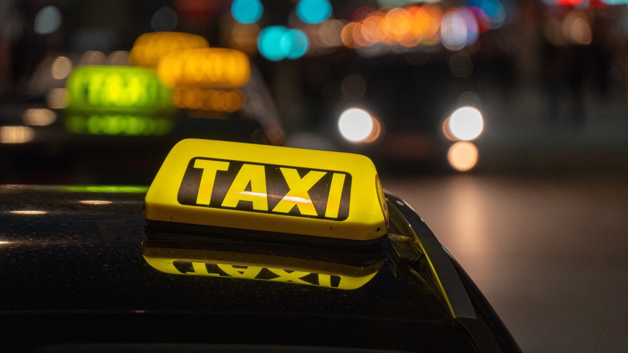 Shallow depth of field image shows classic taxi signs illuminating a pitch-black city at night.