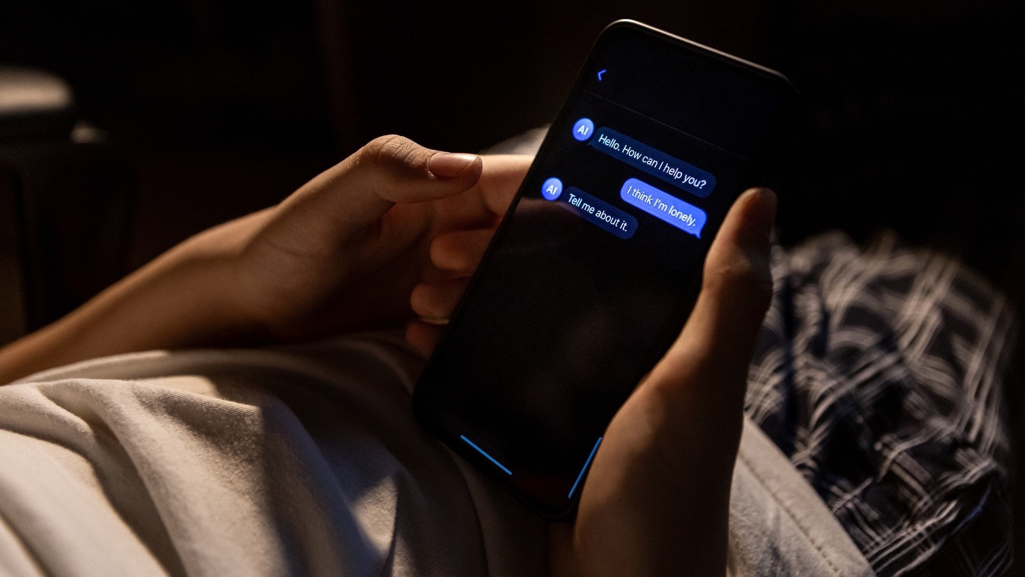 Teen holding smartphone with chat conversation on screen late at night at home. Scene represents digital communication, online interaction and private mobile messaging.