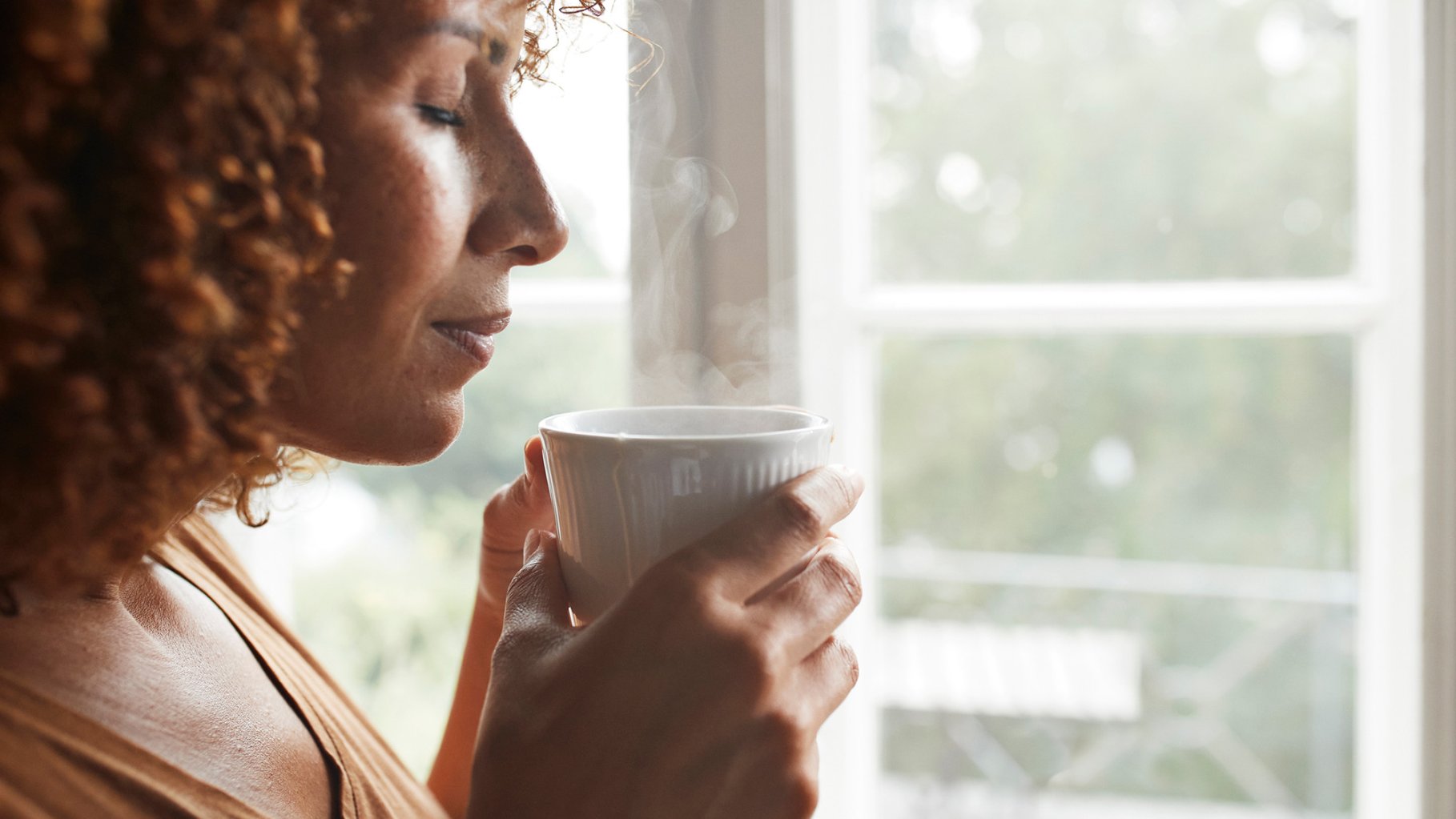 Mature POC woman smelling coffee at home