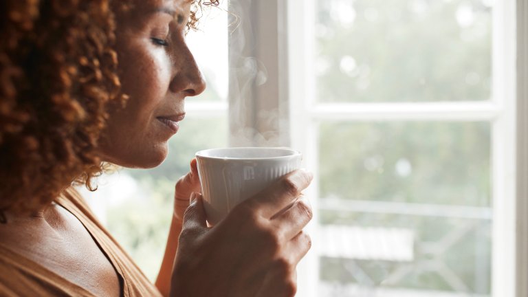 Mature POC woman smelling coffee at home