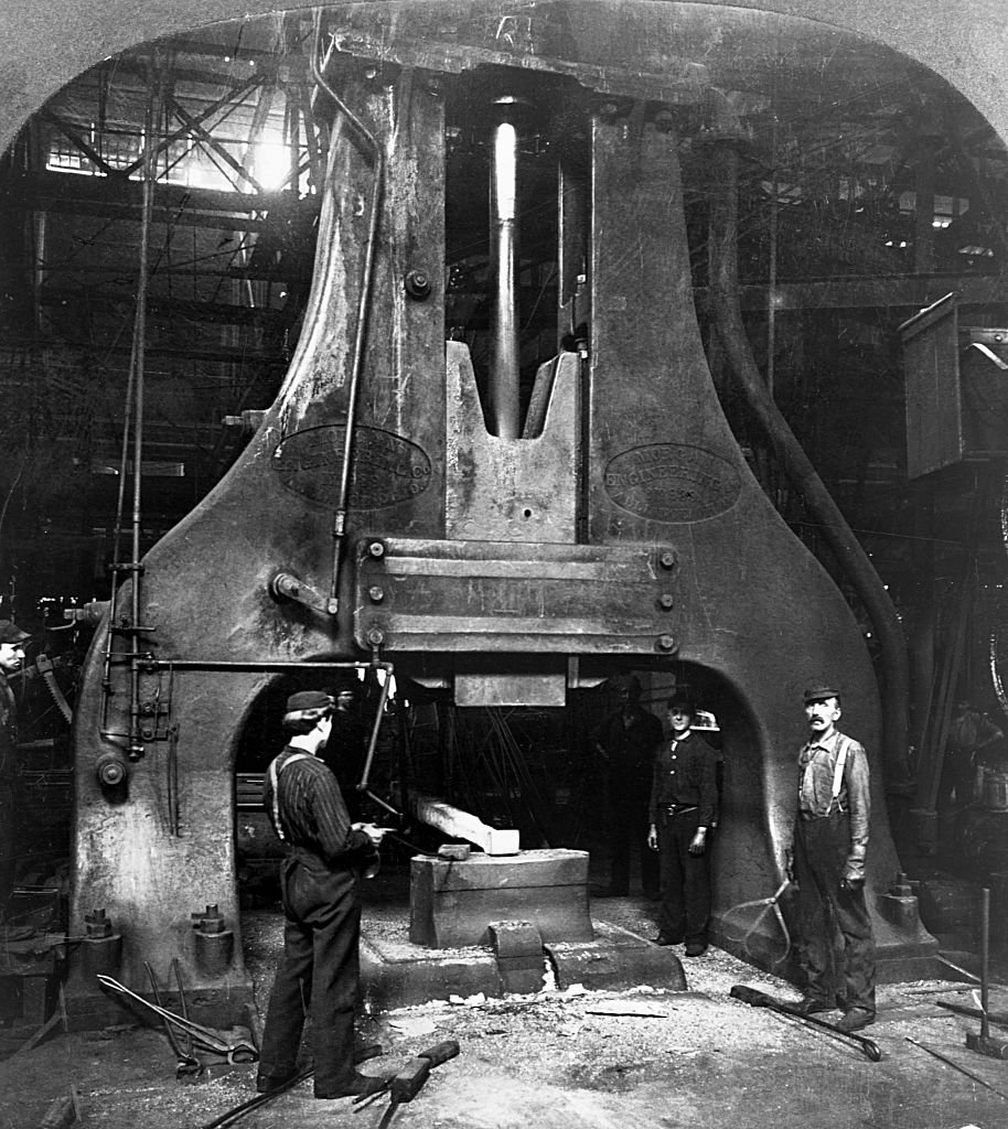 Steel workers stand next to the trip hammer in a steel mill. (Photo by © CORBIS/Corbis via Getty Images)
