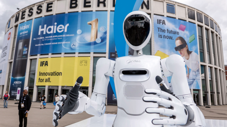 a white, humanoid robot stands in front of a circular convention center