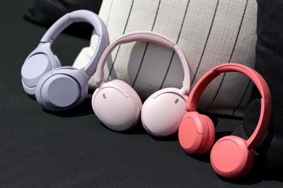 Sony's new WH-1000XM4C in lavender, WH-CH730N in pink, and WH-CH530 in coral on a black and white pillow.