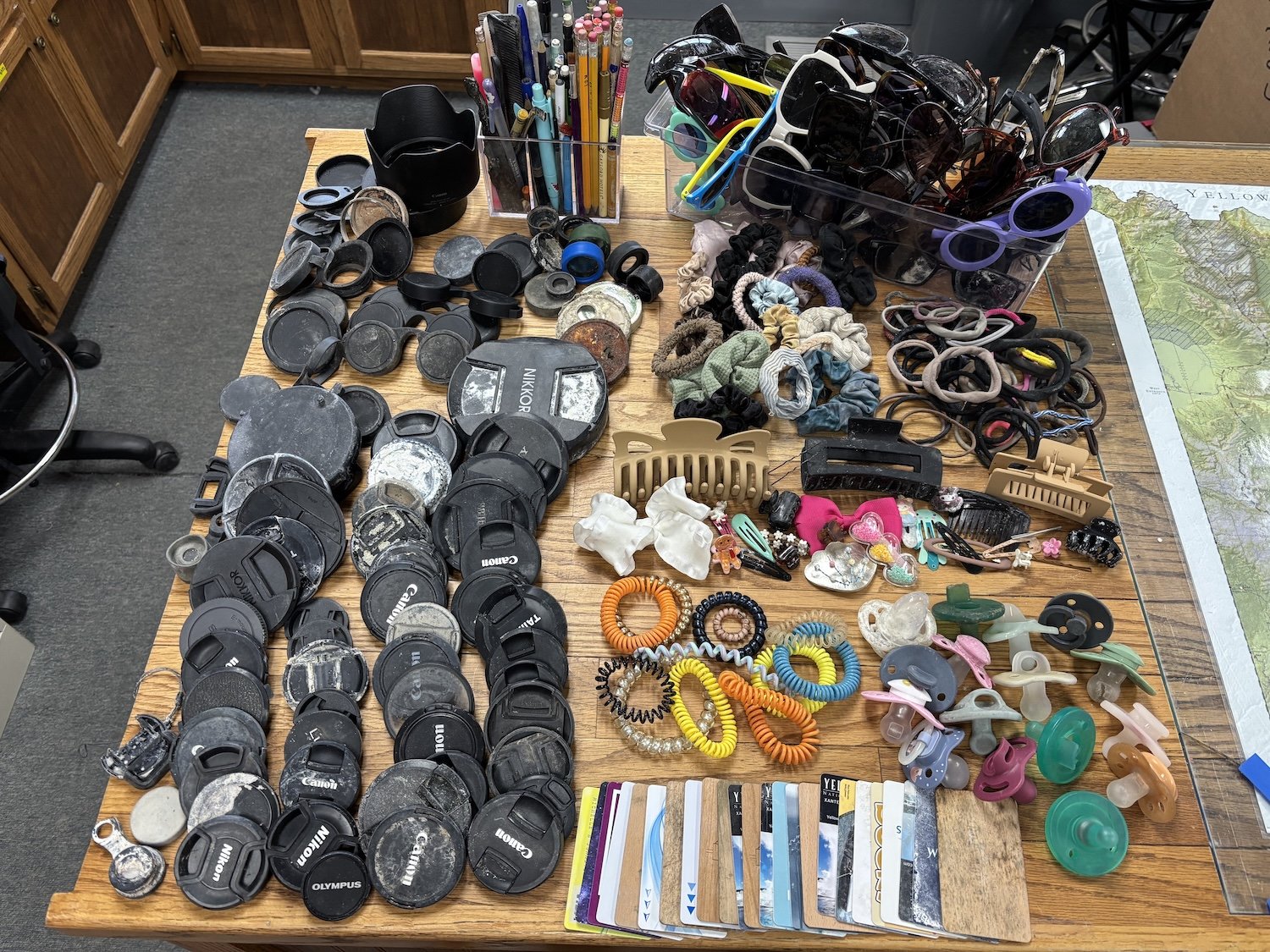 Table of random items retrieved from Yellowstone park including camera lens caps, pacifiers, hair ties, and sunglasses
