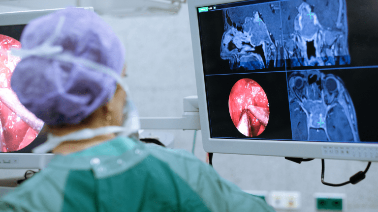 a surgeon in green scrubs points to a screen with x-ray images of the brain
