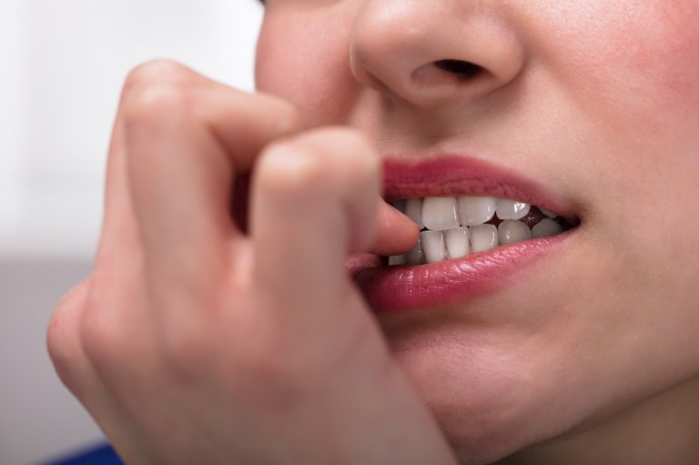 A close-up of a woman's mouth as she bites her fingernails
