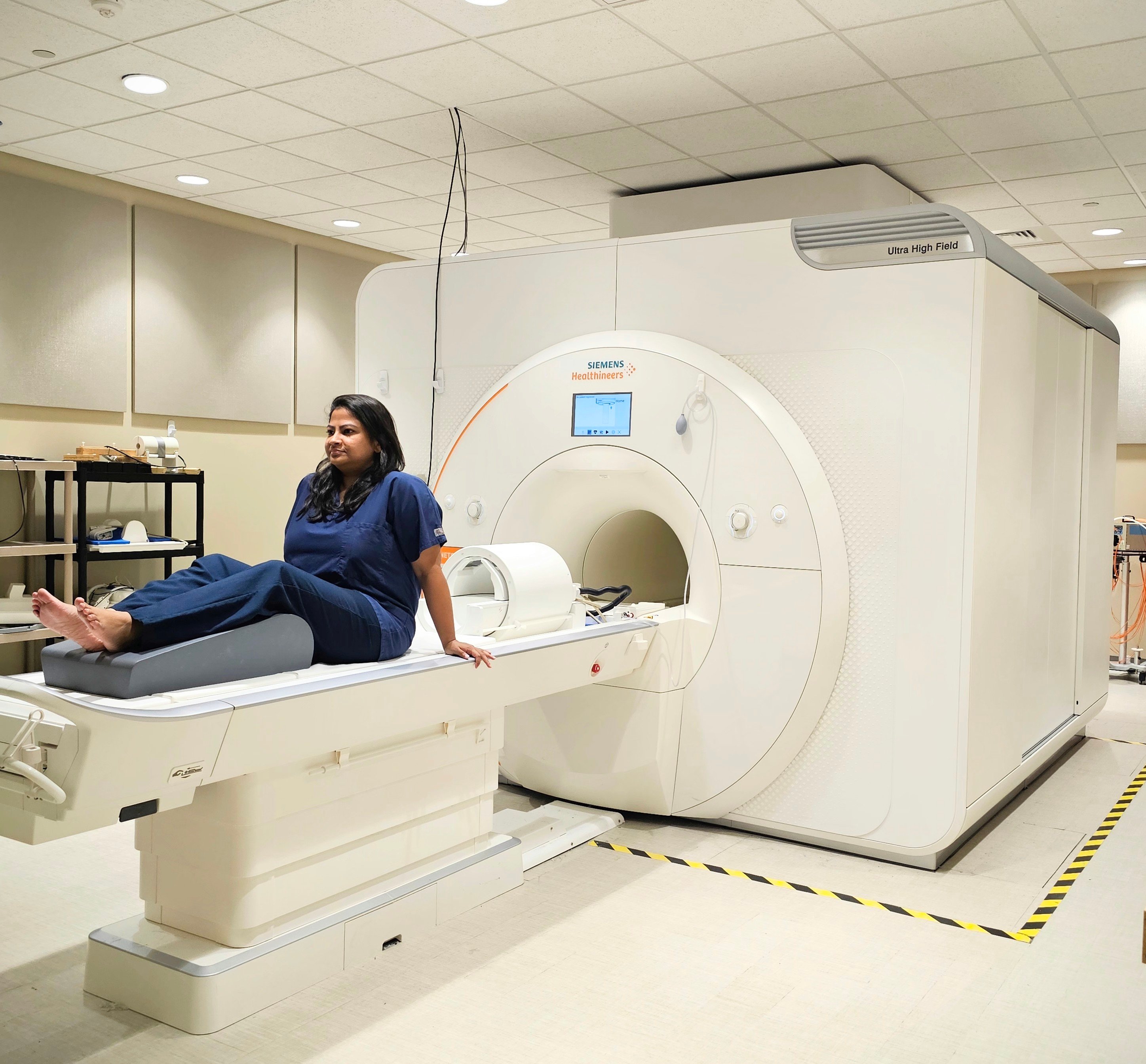 a woman wearing blue scrubs sits outside of an MRI machiene