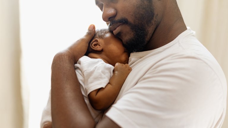 Childcare concept. Loving and caring African American father giving a hug to his newborn baby daughter at home, young black father spending time with his cute little daughter, in the living room, copy