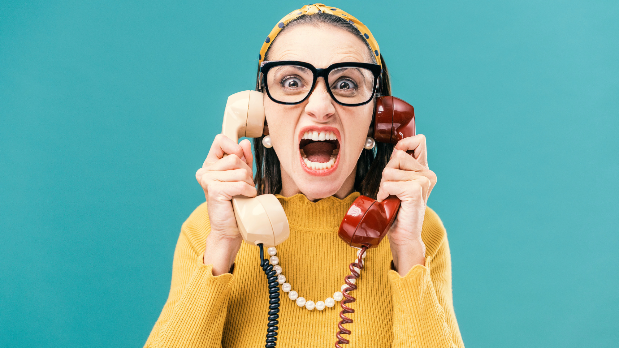 a woman holds two old fashioned phones up to her ears and yells