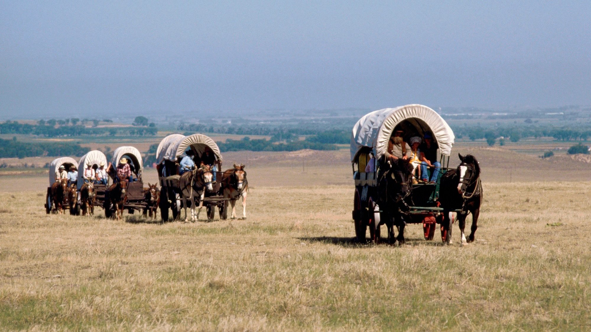 Vacationers ride in covered wagons across the Nebraska prairie along the route of the Oregon Trail as part of a vacation to simulate the Oregon Trail experience. Near Bayard, Nebraska. | Location: near Bayard, Nebraska, USA. (Photo by James L. Amos/Corbis via Getty Images)