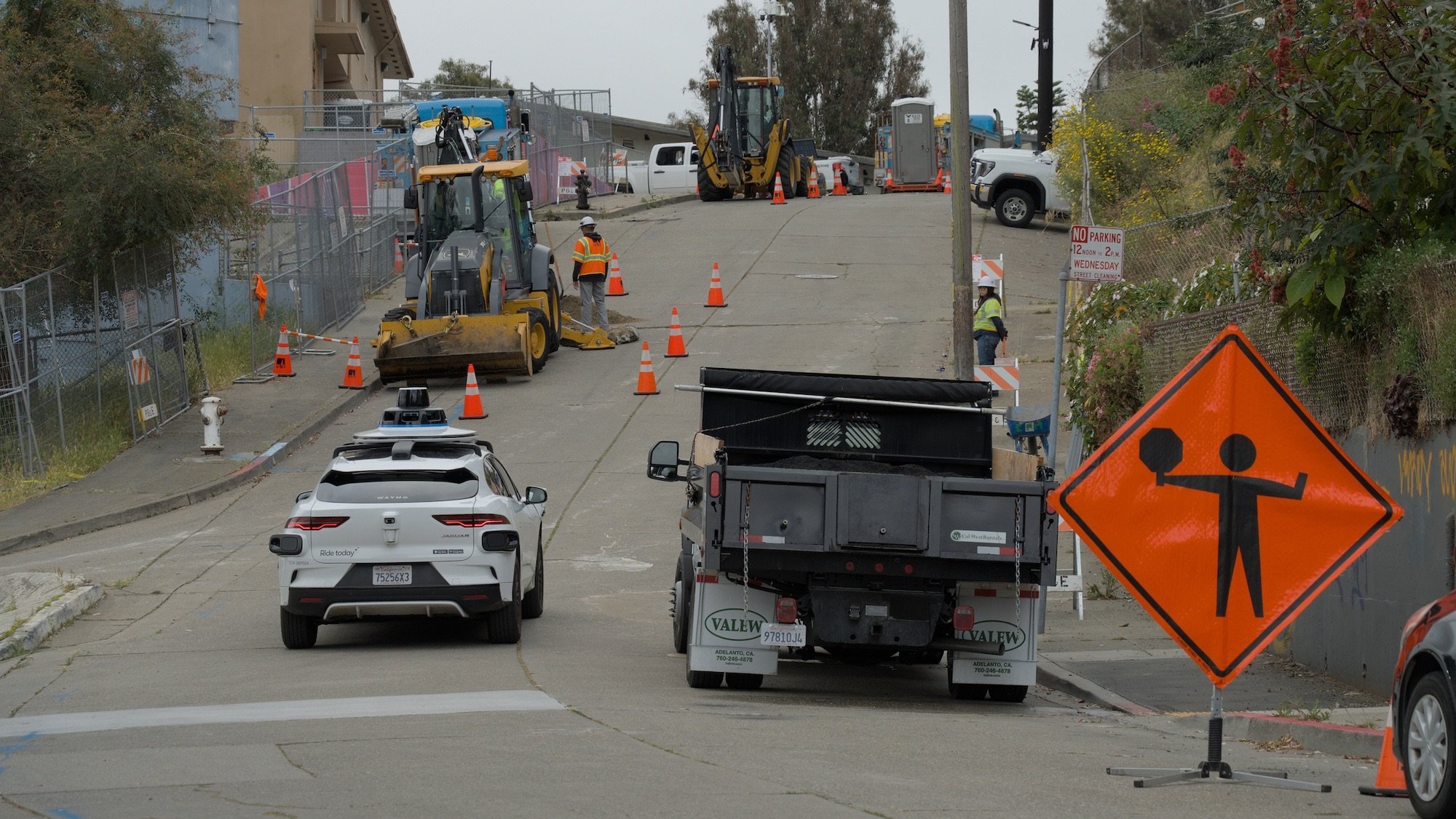 An autonomous Waymo car drives into the blocked off Potrero Annex construction site while a construction worker watches.