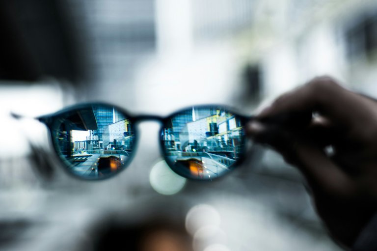 Seeing the world refracted through a pair of glasses being held up by their arm