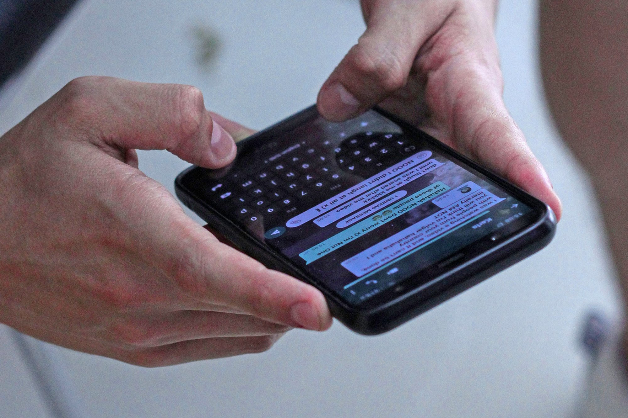 Two hands holding a smartphone that's showing a messaging app, probably WhatsApp