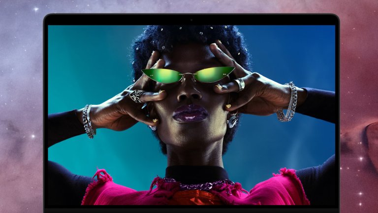 A space black 14-inch MacBook Pro with M6 displaying a vivid portrait of a woman wearing green sunglasses.