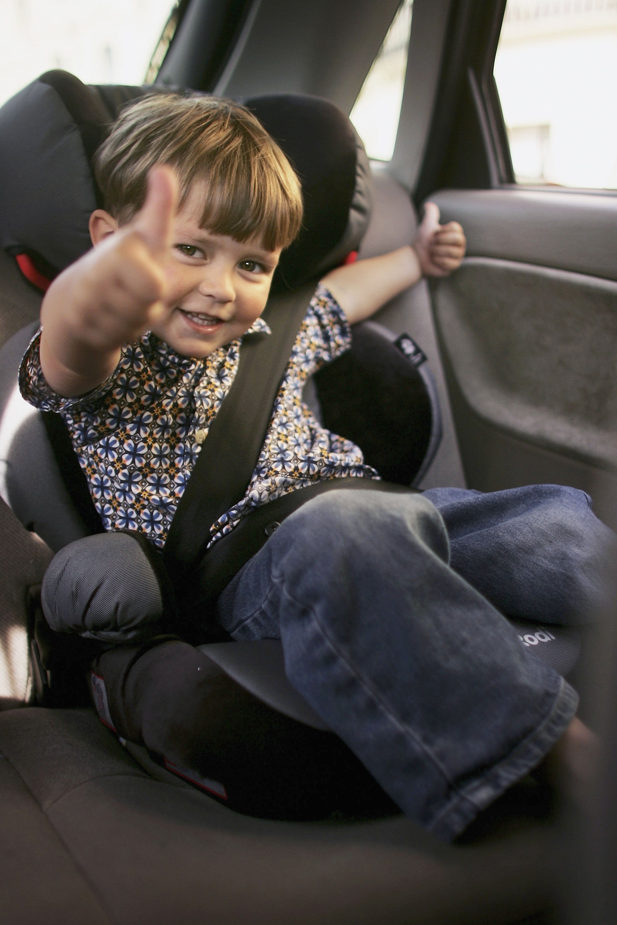 Toddler gives thumbs up from car seat.