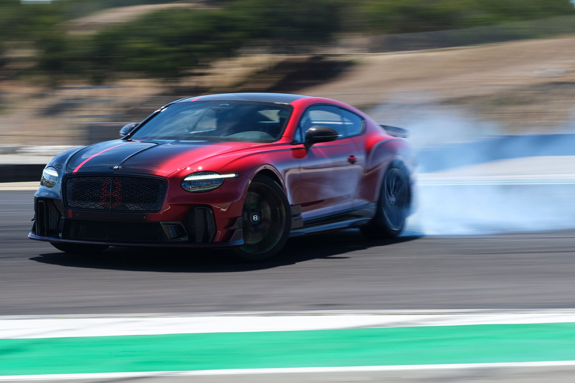 A Bentley 2026 Supersports car shown in Design by Mulliner ombré paintwork fading from Dragon Red II to Black Crystal, drifting on a racetrack in Monterey, California.