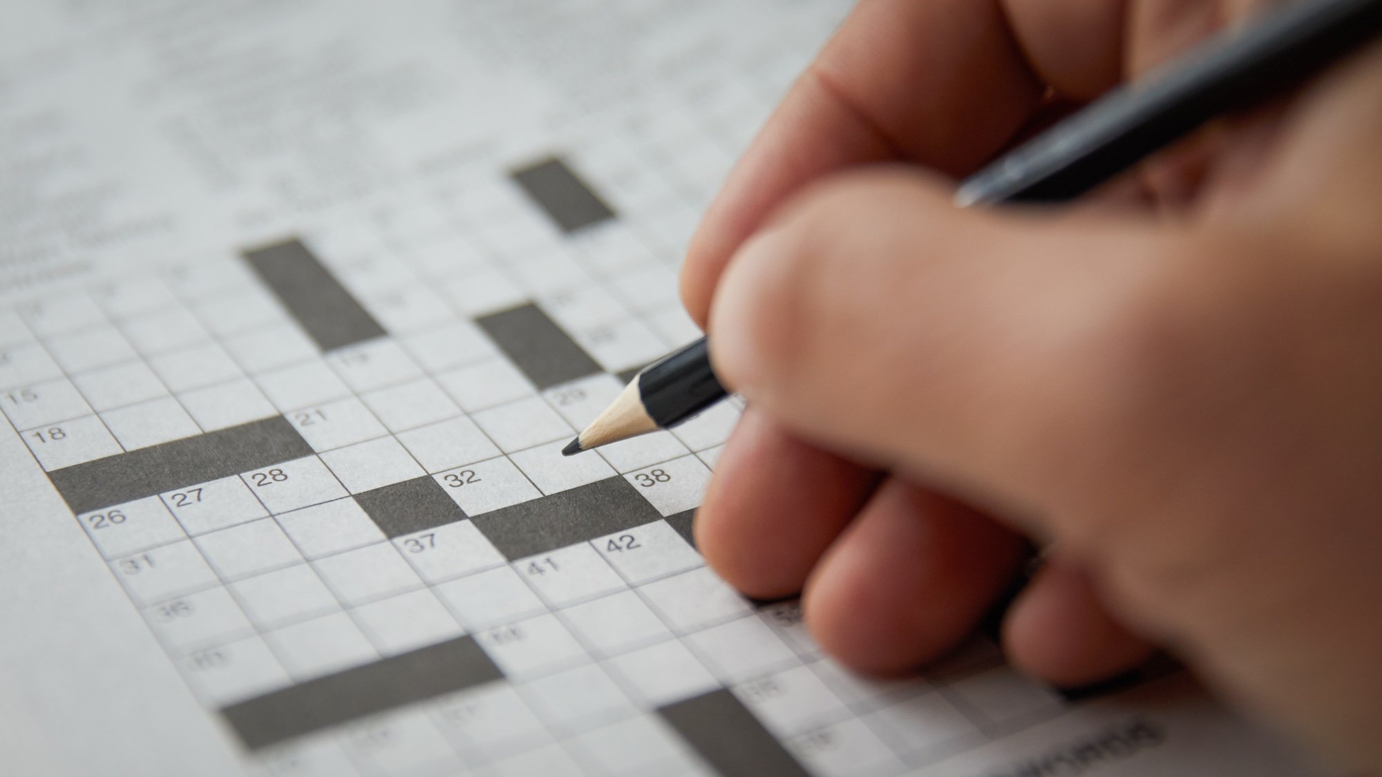 Close up of hand solving a blank crossword puzzle