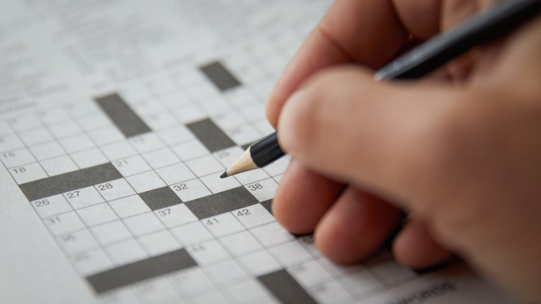 Close up of hand solving a blank crossword puzzle