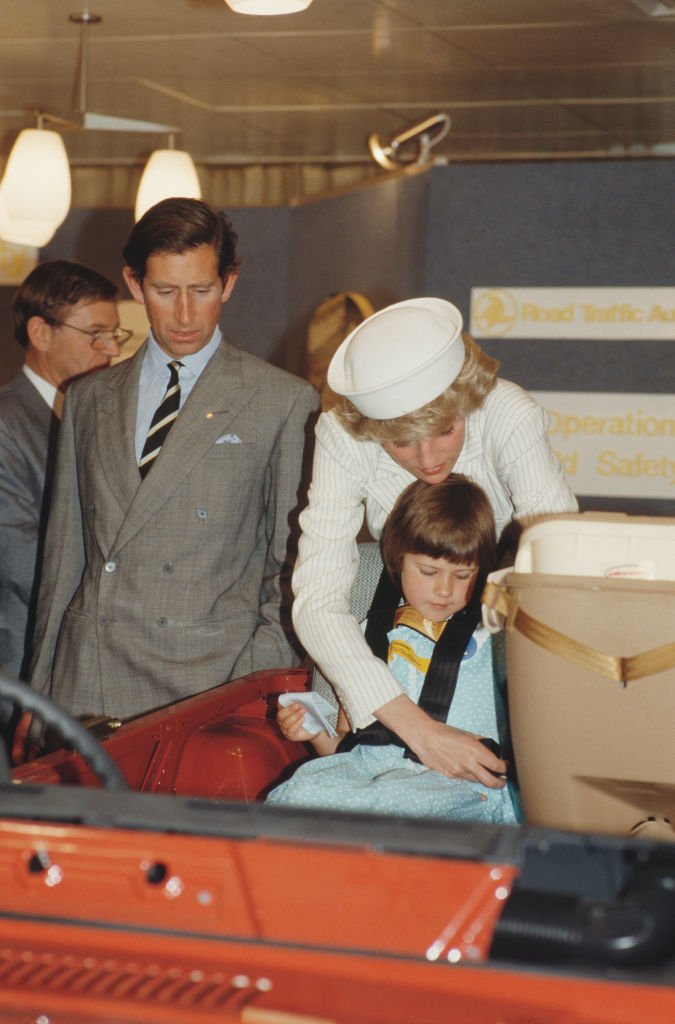 Princess Diana buckle a girl into a car seat and Prince Charles looks on in hospital photo opportunity.
