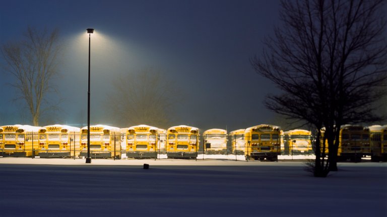 Line of school buses in parking lot on a snowy evening