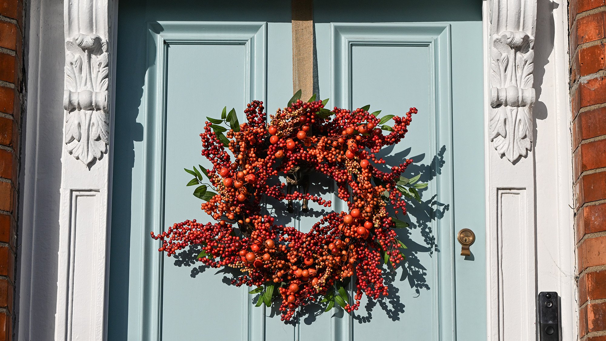 An autumn wreath crafted from red berries and orange rosehips hangs from a powder-blue wooden entry door.