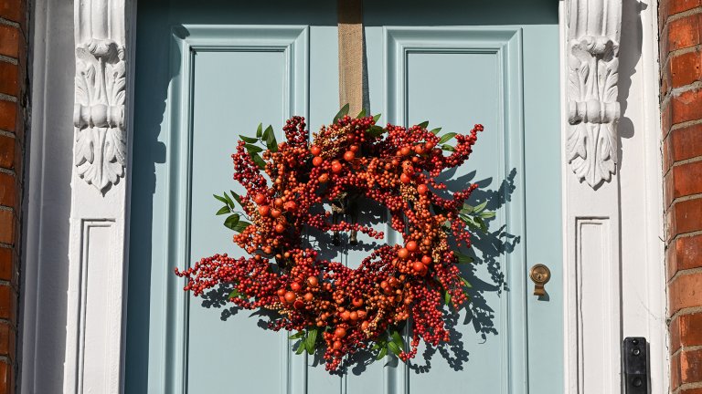 An autumn wreath crafted from red berries and orange rosehips hangs from a powder-blue wooden entry door.