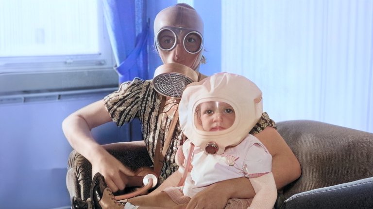 Woman and child wearing gas mask in arm chair.