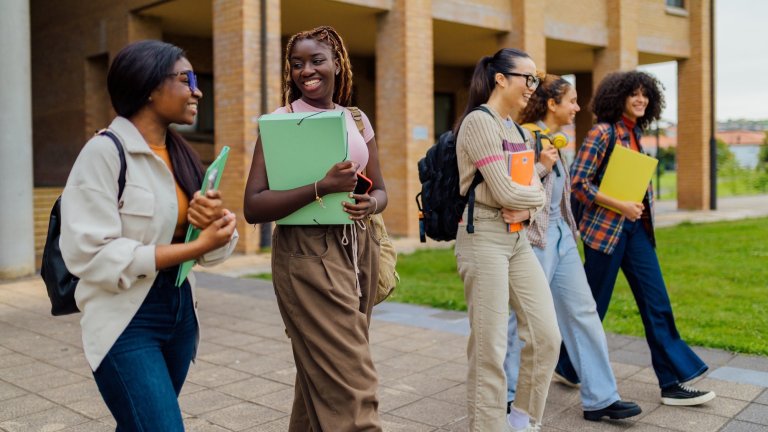 Multiracial group of female students walking together on a university campus, carrying books and backpacks