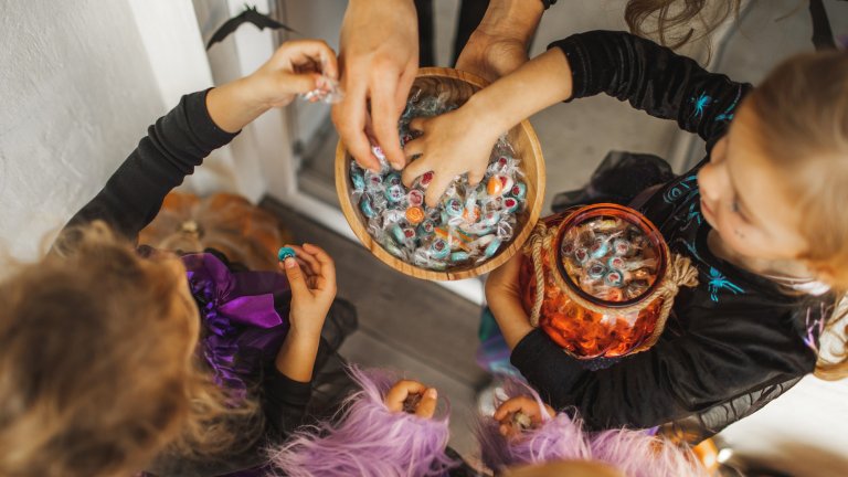 Two little girls in costumes grab candy from a wooden ball in a top down photograph.