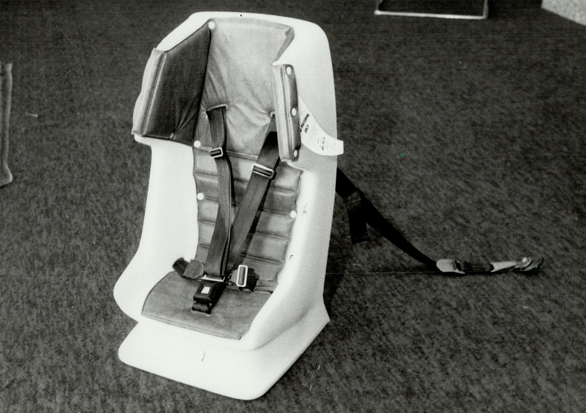 Vintage, black and white photograph of a child's car seat with seat belt and tether.